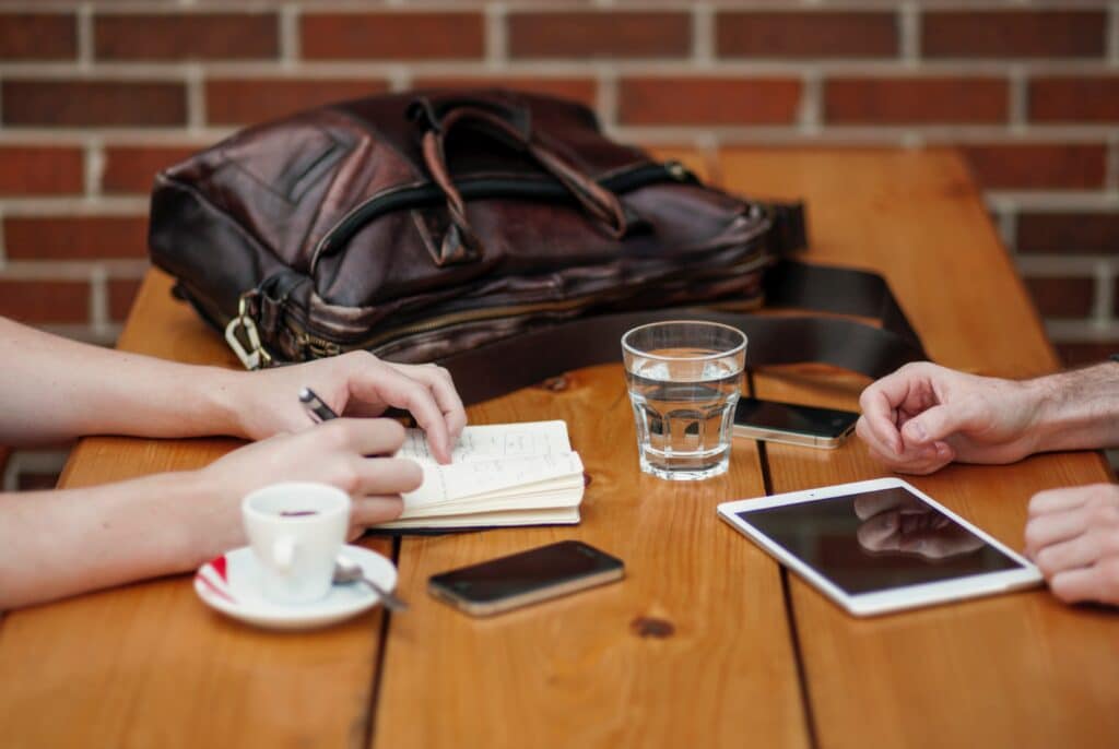 Two cups of coffee on a table and two sets of hands near them.