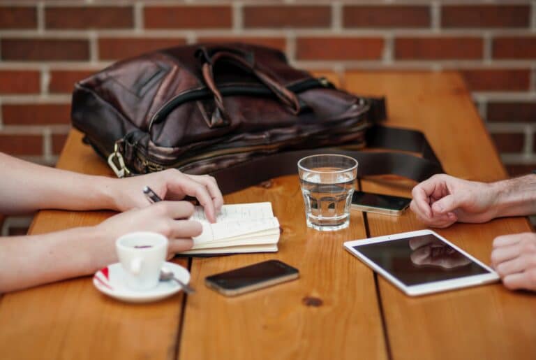 Two cups of coffee on a table and two sets of hands near them.